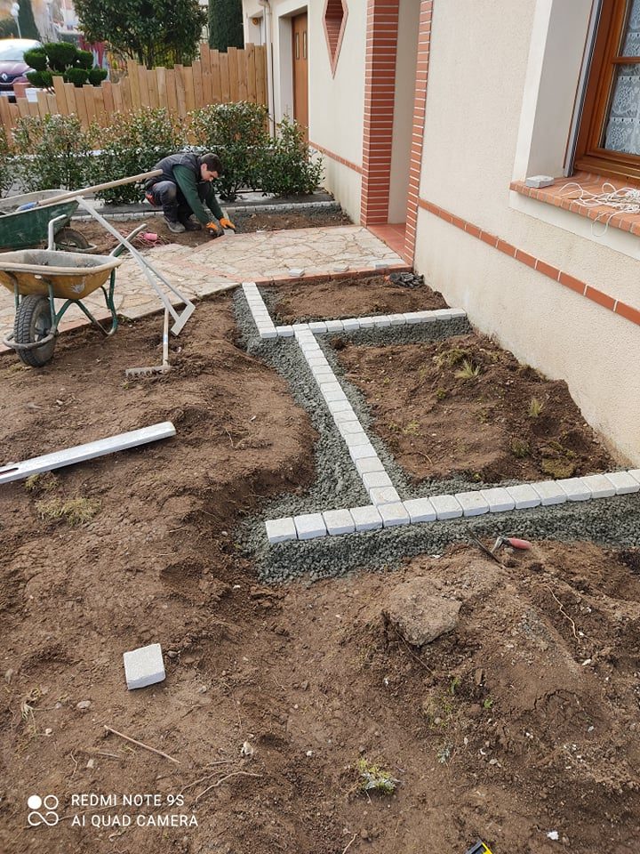 Aménagement de la devanture d'une maison avec un parterre contenant des massifs de plantes et des graviers ainsi qu'un chemin en carrelage